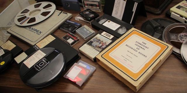 desk with several books, cassettes, VHS, and reel-to-reel tapes
